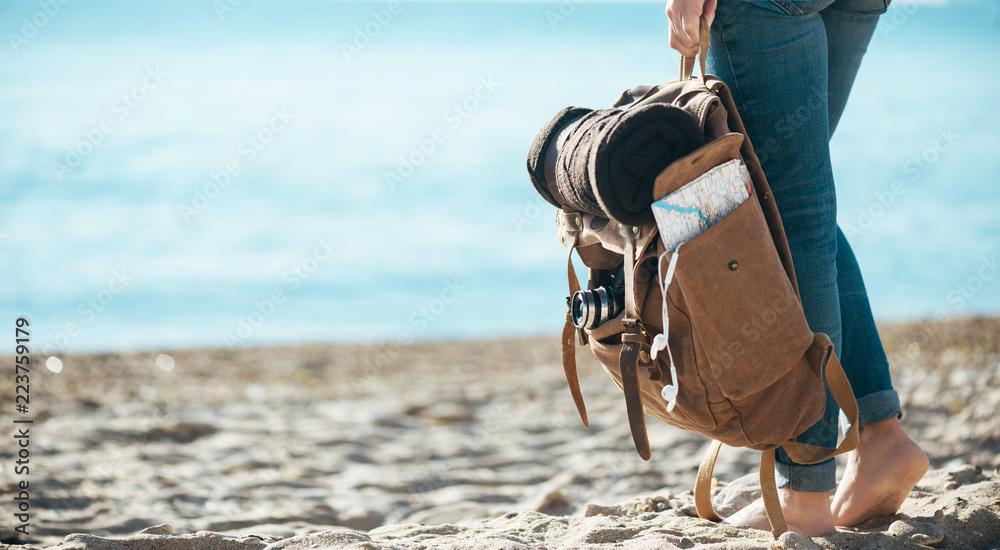Woman traveler stand on the sand beach and holding backpack. Concept of travel. - obrazy, fototapety, plakaty 