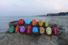 Happy Birthday Message With Multi Colored Stones Over Two Pieces Of Wood With Sea Background