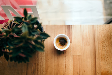 Wall Mural - cup of coffee next to a window and a flower in a cafe shop. Morning fresh coffee