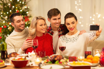 Wall Mural - holidays and celebration concept - happy friends taking selfie by smartphone at home christmas dinner