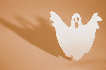 Halloween background concept. Funny ghost doing boo gesture and graphic shade behind on orange table.