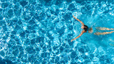 Fototapeta  - Aerial drone view of active girl in swimming pool from above, yong woman swims in blue water, tropical vacation, holiday on resort concept
