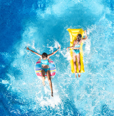 Wall Mural - Aerial drone view of children in swimming pool from above, happy kids swim on inflatable ring donut and mattress, girls have fun in water on family vacation on holiday resort
