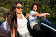 © Leika production - Gorgeous young dark-haired woman in sunglasses with young man are sitting in a black cabriolet on a sunny day.