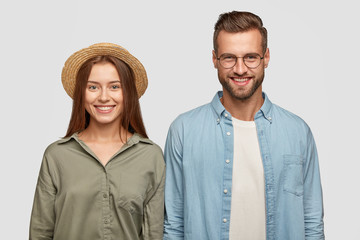 Wall Mural - Isolated shot of happy friends enjoy pastime together, have toothy smiles, rejoice positive moments, stand closely against white studio wall. Glad woman in straw hat and her boyfriend have date