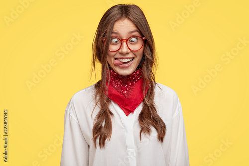 Photo of crazy girlfriend makes funny face, crosses eyes and sticks out tongue, plays fool, doesnt want to be responsible, being in good mood, models indoor against yellow studio background Tableau sur Toile