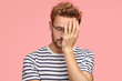 © wayhome.studio - Tired overworked curly ordinary man keeps hand on face, closes eyes, feels sleepy after working all night, dressed in striped t shirt, isoated over pink studio wall. Fatigue freelancer needs rest.