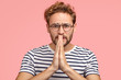 © WHstudio Leushin N - Miserable man with begging expression, asks for favor, keeps hands in praying gesture, wears stirped t shirt, stands against pink background. Please, cover me at work! Body language concept.