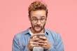 © wayhome.studio - What does it mean? Clueless surprised handsome European guy looks with confusion at camera, recieves strange reply under post, connected to wireless free internet, isolated over pink background