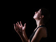 Low key of a faithful woman praying and feeling the presence or being touched by god. Arms outstretched in worship, head up and eyes closed in religious fervor. Black background.