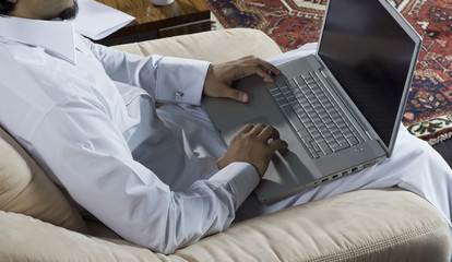 Wall Mural - Mideastern man using laptop at home, with a cup of cofee and documents