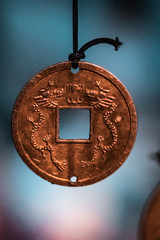 Oriental, magical pendants. Traditional asiatic and chinese currency, transformed into fortune coins with powerful engravings. Bronze, copper, gold necklace, black thread, blurry background. 