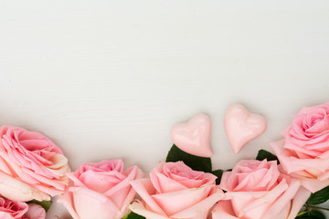 Rose fresh flowers border with two hearts on light table from above with copy space, flat lay scene