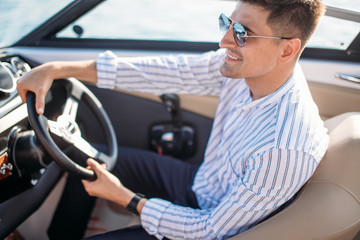 Wall Mural - Serious handsome business man dressed in classy style, with sunglasses relaxing during sailing on river, he sitting begins the helm and driving it on full speed.