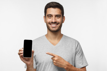 Wall Mural - young smiling man holding blank phone with empty black screen, isolated on gray background