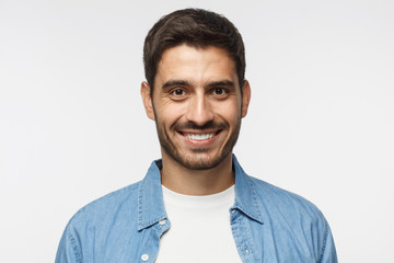 Headshot of young handsome man isolated on gray background, wearing casual blue shirt, smiling happily and friendly at camera