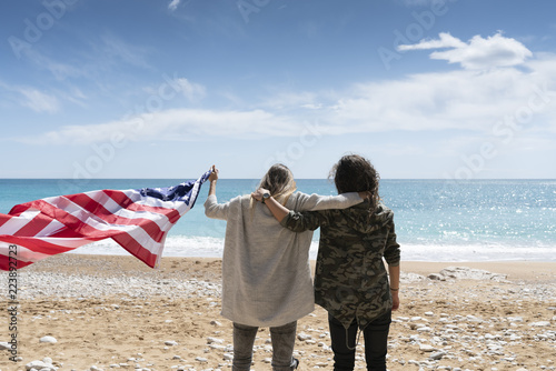 Photographie Two girls holding United states of America flag in beach