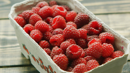 Closeup container full of fresh ripe red raspberry on wooden background 