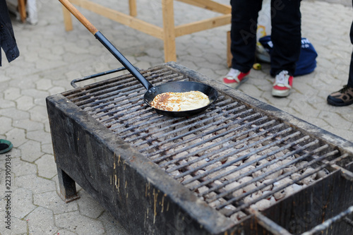 Fotografía Process of cooking pancakes on frying pan on bonfire during carnival