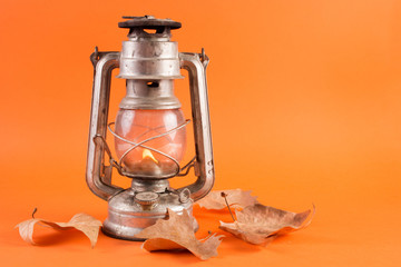 Old retro gas lantern with burning light and fallen dry leaves isolated on orange background. Autumn concept. Close up, selective focus