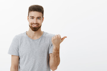 Waist-up shot of handsome stylish and masculine self-assured male with beard and white cute smile pointing right with thumb assuring copy space is perfect with confident delighted expression