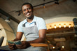 Young cheerful man in apron looking at you with toothy smile while counting money