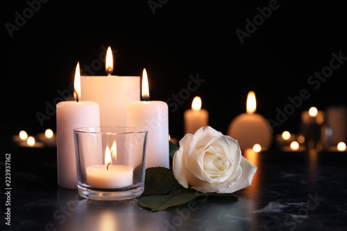 White rose and burning candles on table in darkness. Funeral symbol © New Africa