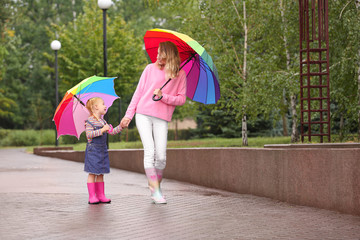 Wall Mural - Happy mother and daughter with bright umbrellas walking in park