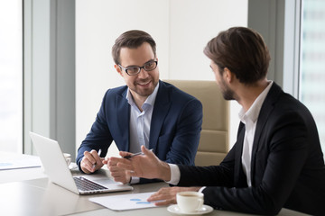 two smiling businessmen working at laptop in office discussing ideas, happy managers or workers talk