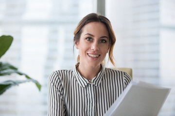portrait of smiling millennial businesswoman holding documents looking at camera, headshot of happy 