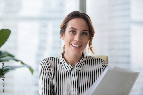 Fotomural Portrait of smiling millennial businesswoman holding documents looking at camera, headshot of happy woman worker or female ceo posing with paperwork making picture at corporate photoshoot