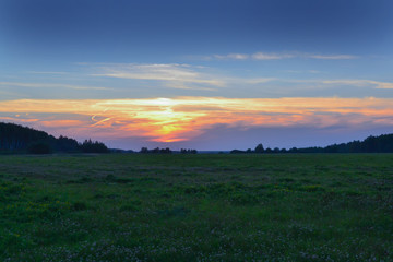 Beautiful sunset in the field. Red, yellow, blue sky. Summer evening.