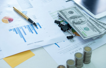 Pen on finance chart document with coins and dollars.