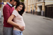 I love everything about you. Portrait of happy gentleman embracing his beautiful pregnant wife and gently touching her belly. Young lady looking down and smiling