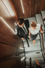 Wall Mural - Top view full length smiling unshaven male going with cheerful lady while talking. They reflecting in mirror