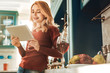 © zinkevych - Enjoy your rest. Joyful woman standing in semi position in kitchen and holding tablet in both hands while checking email