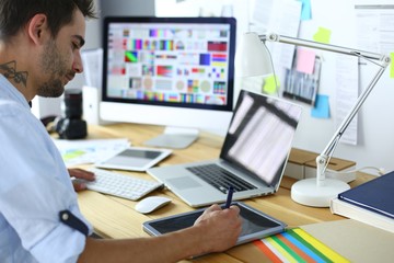 Fototapete - Portrait of young designer sitting at graphic studio in front of laptop and computer while working online.