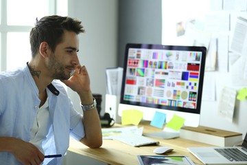 Fototapete - Portrait of young designer sitting at graphic studio in front of laptop and computer while working online.