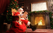 Portrait Of Happy Santa Claus Sitting At His Room At Home Near Christmas Tree And Reading Christmas Letter Or Wish List.