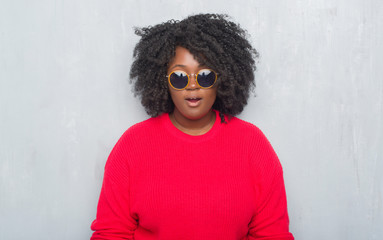 Poster - Young african american plus size woman over grey grunge wall wearing retro sunglasses afraid and shocked with surprise expression, fear and excited face.