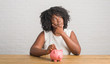 © Krakenimages.com - Young african american woman sitting on the table holding piggy bank serious face thinking about question, very confused idea