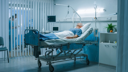 In the Hospital Senior Patient Rests, Lying on the Bed. Recovering Man Sleeping in the Modern Hospital Ward.