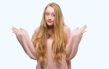 Poster - Blonde teenager woman wearing pink sweater clueless and confused expression with arms and hands raised. Doubt concept.