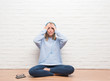 © Krakenimages.com - Beautiful young woman sitting on the floor listening music wearing headphones at home stressed with hand on head, shocked with shame and surprise face, angry and frustrated. Fear and upset