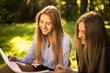 © Sunrise Team - Young beautiful ladies students sitting in the park outdoors on grass holding copybook doing homework.
