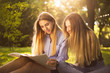 © Sunrise Team - Young beautiful ladies students sitting in the park outdoors on grass holding copybook doing homework.