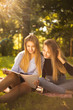 © Sunrise Team - Young beautiful ladies students sitting in the park outdoors on grass holding copybook doing homework.