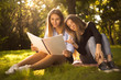 © Sunrise Team - Young beautiful ladies students sitting in the park outdoors on grass holding copybook doing homework.