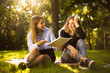 © Sunrise Team - Excited girl try to force her displeased confused friend sister to education students sitting in the park outdoors on grass holding copybook doing homework.