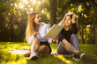 © Sunrise Team - Excited girl try to force her displeased confused friend sister to education students sitting in the park outdoors on grass holding copybook doing homework.